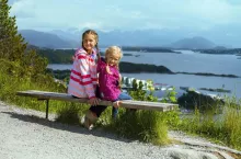 two girls sisters sitting on a bench in the town of Alesund and the mountains to the fjord in the background, norway