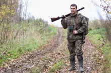 A man in camouflage and with guns in a forest belt on a spring hunt
