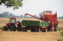 Kombajn i ciągnik z przyczepą podczas żniw.