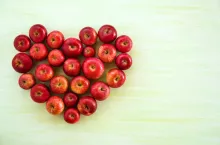 A heart from ripe red apples on the green wooden background, top view.