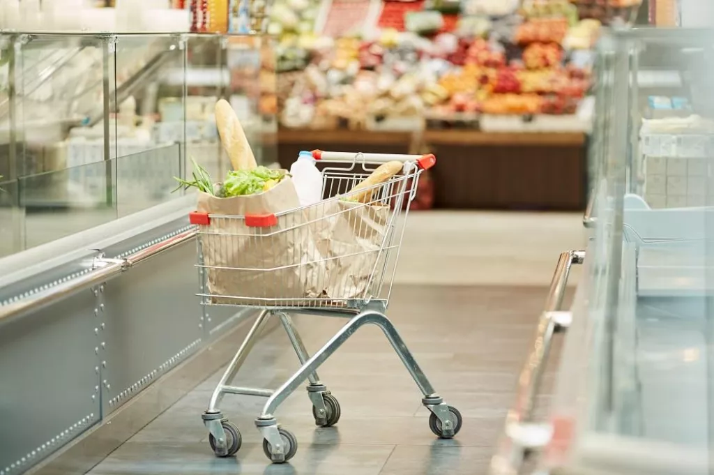 Full length background image of shopping cart with groceries standing in supermarket, copy space