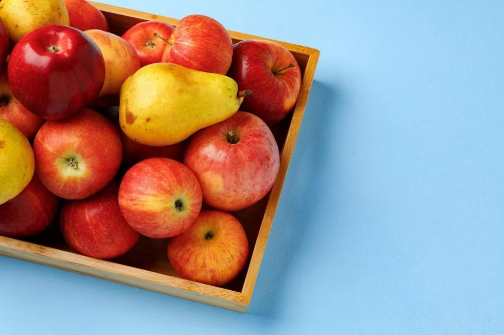 Wooden box with apples and pears on blue background top view