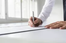 Businessman in white shirt signing contract, document or legal papers in a bright office.