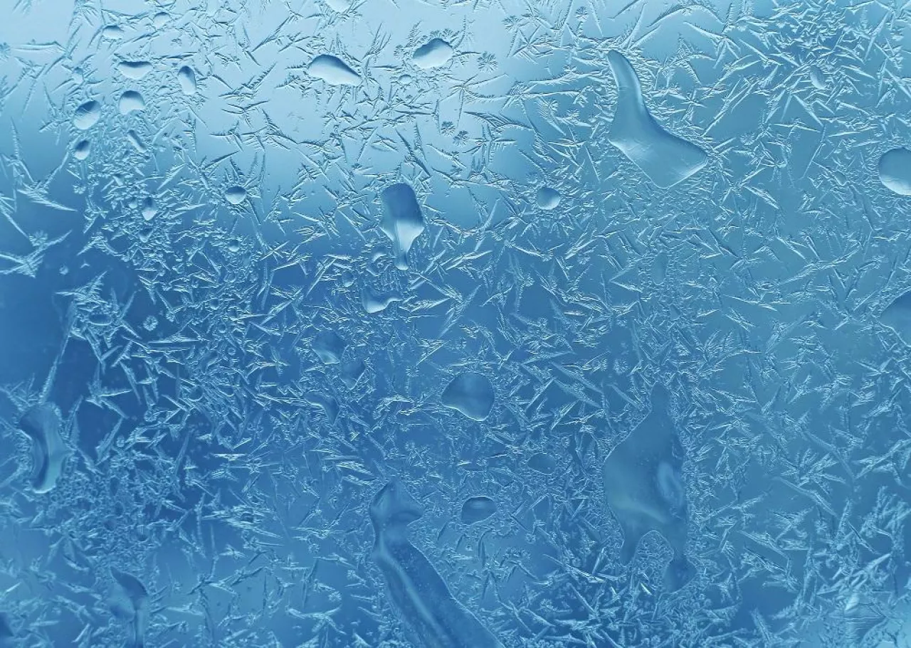 Natural ice pattern and water drops on winter window glass