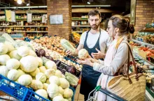 Shop worker helping young woman client to chooose vegetables in the supermarket