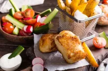 Fish and chips. Fried fish fillet with homemade baked potatoes and fresh salad on wooden cutting board.