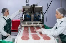 Female butcher processing hamburger patty at meat factory