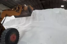 Large pile of white urea fertilizer, stored in the warehouse, waiting for delivery with big yellow loader to deliver to customers