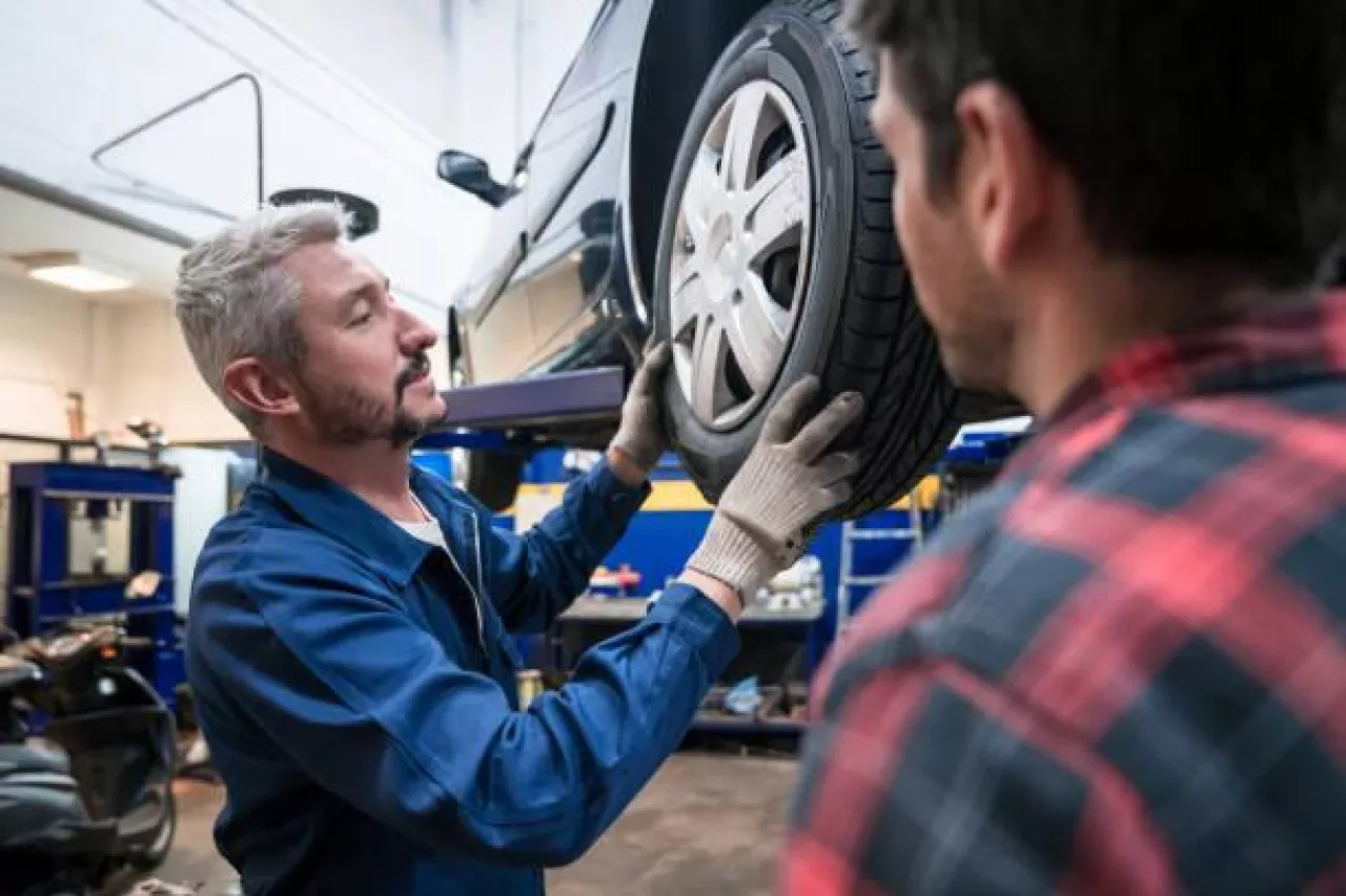 &lt;p&gt;Car mechanic changing car wheel in the auto repair shop, customer talking with him.&lt;/p&gt;