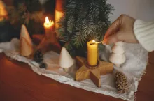 &lt;p&gt;Hand lighting up christmas candle on background of pine trees decorations, cones and rustic cloth on wooden table in evening scandinavian festive room. Holiday advent. Atmospheric winter time&lt;/p&gt;