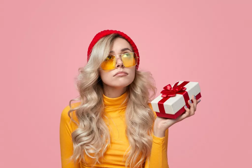 &lt;p&gt;Disappointed young woman in trendy outfit holding unwanted gift box and looking up during holiday celebration against pink background&lt;/p&gt;