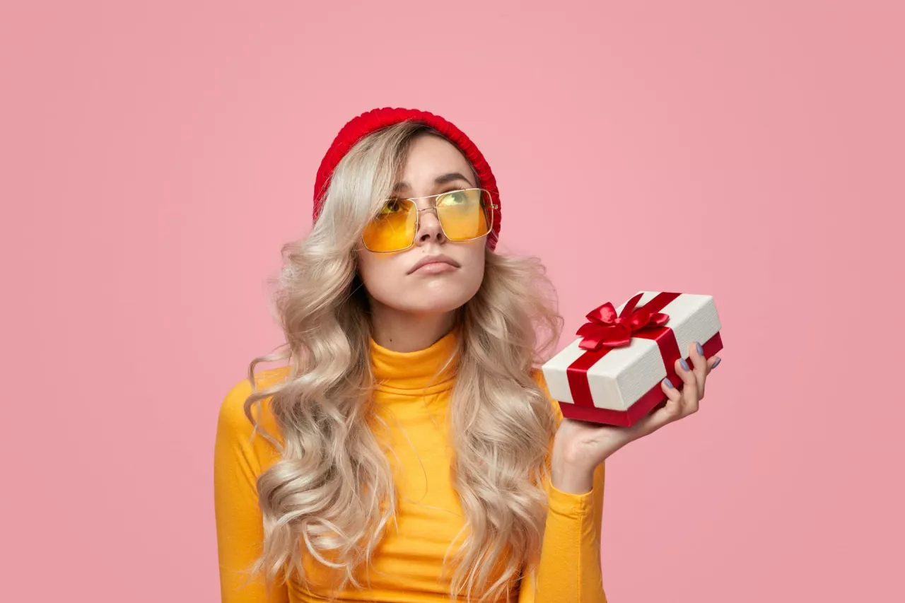&lt;p&gt;Disappointed young woman in trendy outfit holding unwanted gift box and looking up during holiday celebration against pink background&lt;/p&gt;