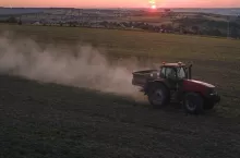 Tractor spraying fertilizers with insecticide herbicide chemicals on agricultural field at sunset.