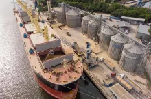 Loading grain into holds of sea cargo vessel in seaport from silos of grain storage. Bunkering of dry cargo ship with grain. Aerial top view