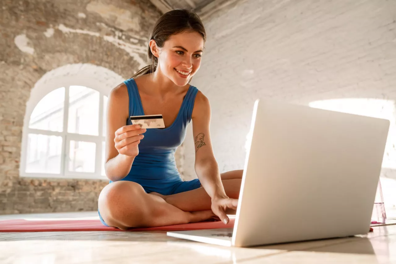 &lt;p&gt;Beautiful smiling sportswoman using credit card and laptop while sitting on mat indoors&lt;/p&gt;