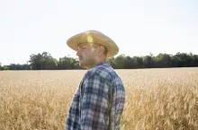 Man wearing a checkered shirt and a hat standing in a cornfield, a farmer.