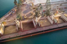 Aerial top view of big cargo ship bulk carrier is loaded with grain of wheat in port at sunset