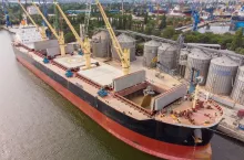 Loading grain into holds of sea cargo vessel in seaport from silos of grain storage. Bunkering of dry cargo ship with grain. Aerial top view
