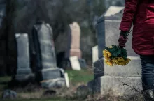 Close-up of a Sad Woman Holding Sunflowers in front of a Loved one‘s Gravestone. Focus on the Bouquet.