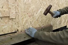 carpenter hitting a long nail with a hammer and hammering it into the structure of a tree in the process of building a wooden structure, driving nails with a hammer during street construction in the countryside