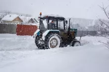During heavy snowfall, the tractor clears the snow-covered road.
