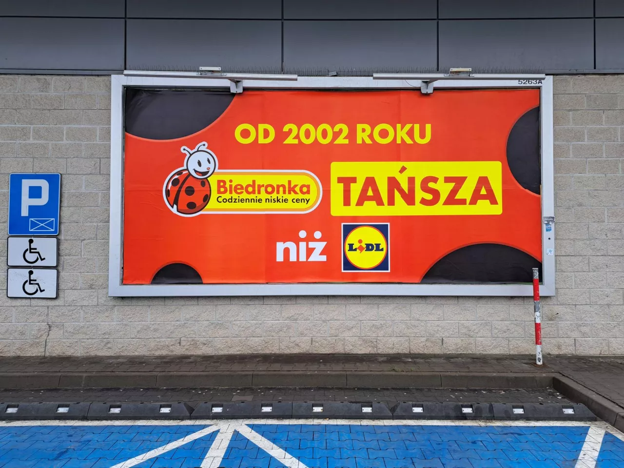 &lt;p&gt;Biedronka informuje na plakatach, że jest tańsza niż Lidl od 2002 roku (fot. wiadomoscihandlowe.pl/MG)&lt;/p&gt;