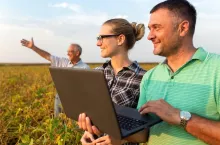 Group of farmers with laptop standing in a field examining soybean crop.