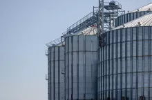 Construction of new cylindrical silos for grain storage. Metal silos are made of corrugated metal. A row of hand winches lifts the metal structure upward. Agribusiness. Grain exports.