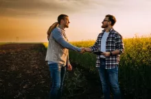 Two business man shake hands on a field.