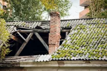 The roof collapsed. Damaged falling roof and chimney on sunny day with clear blue sky.