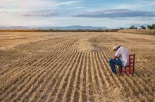 Farmer with straw hat and hoe sitting on a red chair in the middle of the field. Agriculture concept.