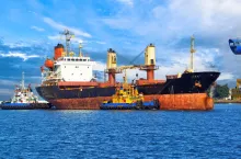 Bulk carrier for transportation of wheat in the waters of the port of Odessa. Two sea tugs moor an old dry-cargo ship in the port of the city of Odessa on the Black Sea, Ukraine