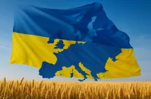 Flaga Ukrainy z naniesionym konturem geograficznym Europy, powiewająca nad dojrzałym polem pszenicy. Niebiesko-żółte barwy flagi oraz kłosie zboża na pierwszym planie nawiązują do symboliki narodowej Ukrainy i jej roli w rolnictwie europejskim.