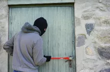 Osoba w kominiarce próbuje wyłamać zamek drzwi łomem.