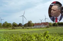 Widok na farmę wiatrową położoną w pobliżu zabudowań wiejskich. Na zdjęciu wmontowany wizerunek prezydenta Karola Nawrockiego, który zapowiedział weto wobec ustawy wiatrakowej.