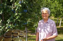 Starsza uśmiechnięta kobieta wstojąća pod drzewem