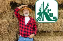 Rolnik stojący na tle sterty bel w jeansach, koszuli czerwonej w czarną kratkę i słomianym kapeluszu