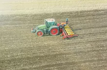 Traktor wykonuje siew na dużym polu uprawnym. Zdjęcie z drona przedstawia pracę maszyn rolniczych podczas wiosennych lub jesiennych zasiewów