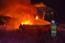 Strażak nocną porą gasi pożar kombajnu na polu