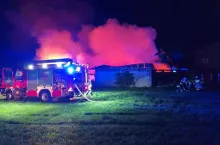 Czerwony wóz gaśniczy straży pożarnej przed palącą się stodołą