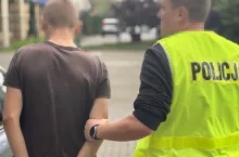 Policjant trzyma za rękę aresztowanego mężczyznę