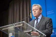 Były komisarz UE ds. rolnictwa przemawia podczas konferencji prasowej przy mównicy z logo Rady Unii Europejskiej. W tle niebieskie tło i flaga UE.