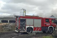 Wóz strażacki z rozwiniętą linią gaśniczą przed palącą się oborą