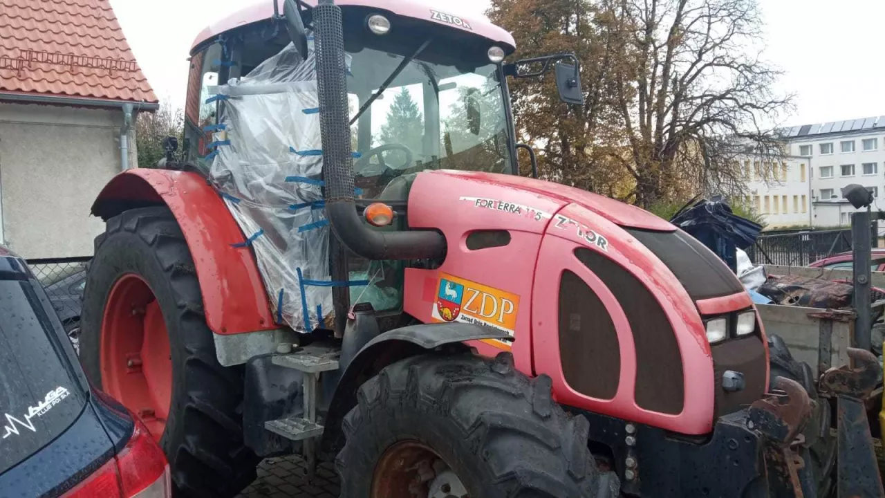Czerwony ciągnik rolniczy na parkingu bez jednego skrzydła drzwi