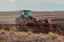Widok na ciągnik z kultywatorem przedsiewnym pracujący na polu uprawnym wczesną wiosną.