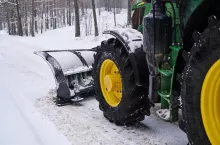 Ciągnik John Deere z pługiem odśnieżający drogę do gospodarstwa sadowniczego