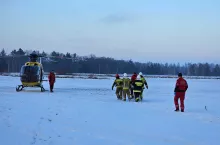 Strażacy na noszach przenoszą ranną kobietę do helikoptera LPR na polu w śniegu