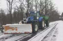 Ciągnik New Holland na zaśnieżonej drodze z zaczepionym pługiem śnieżnym