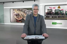 Mężczyzna w szarej marynarce przed mównicą z rozłozoną gazetą