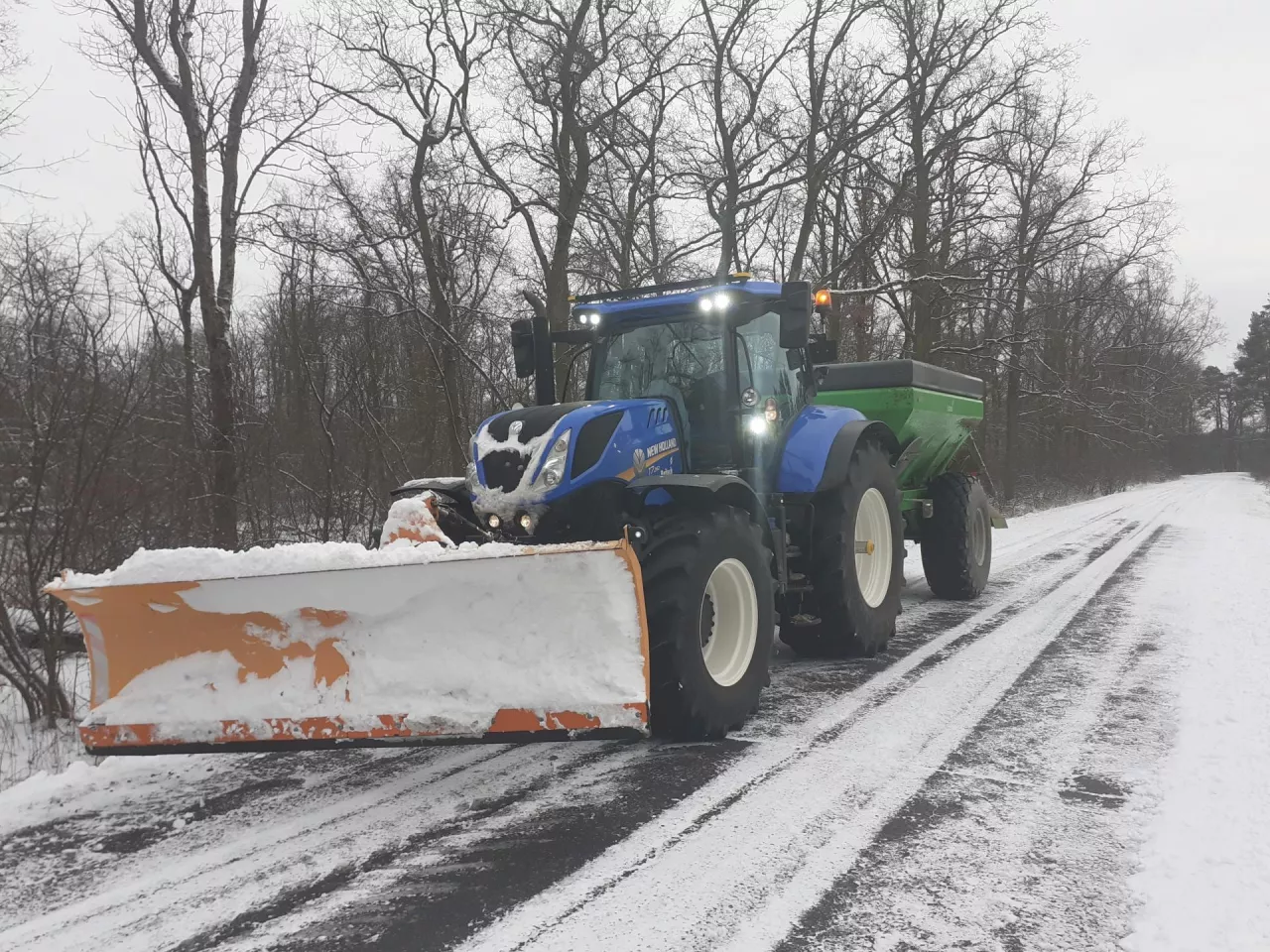 Ciągnik New Holland na zaśnieżonej drodze z zaczepionym pługiem śnieżnym